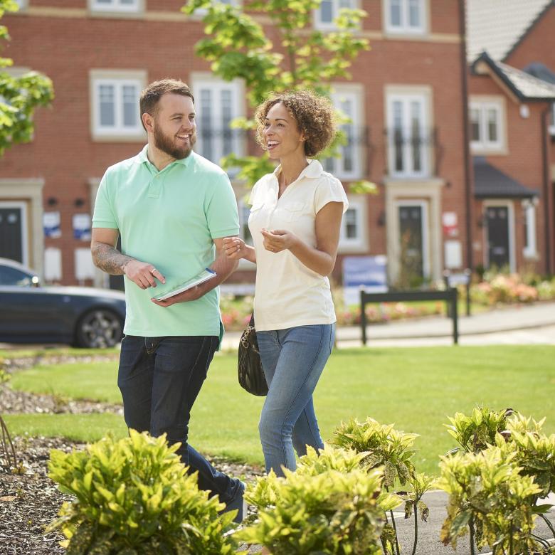 A happy couple walking through a new-build estate on their way to view a new house